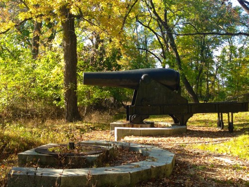 A historic cannon on a stone platform surrounded by trees with autumn foliage.