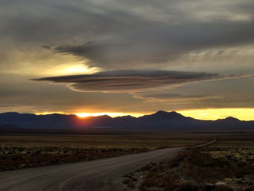 A dramatic sunset behind mountains, featuring a unique lenticular cloud hovering above the horizon.