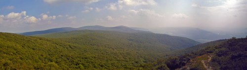 Panoramic view of lush green mountains under a cloudy sky, with a winding path visible in the foreground.