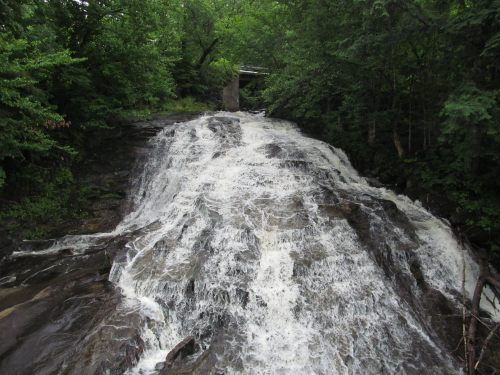 A cascading waterfall flows over rocky terrain, surrounded by lush green trees and foliage.