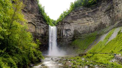 A majestic waterfall cascades down rocky cliffs, surrounded by lush greenery and a serene river below.