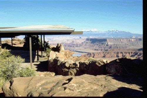 A scenic view of a canyon with mountains in the background, featuring a modern structure on the edge of the cliff.