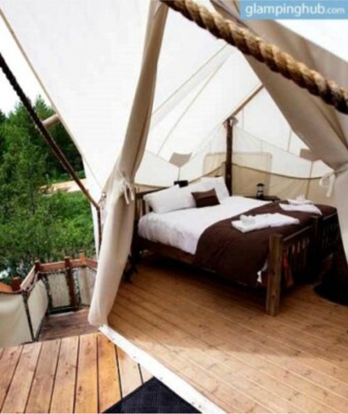 Cozy glamping tent interior with a wooden bed, white linens, and a view of nature through the open entrance.