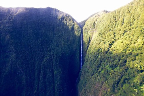 A stunning waterfall cascading down a lush green mountain surrounded by steep cliffs and dense vegetation.