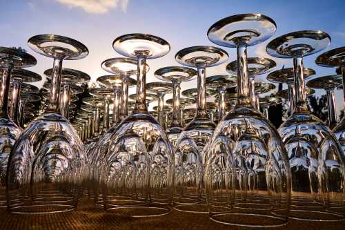 A close-up of stacked glass wine glasses reflecting sunlight against a blue sky.