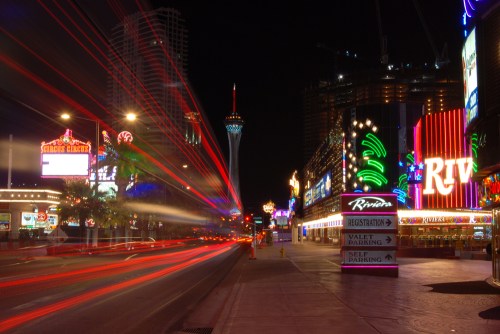 Vibrant Las Vegas Strip at night, featuring neon lights, busy streets, and the Stratosphere tower in the background.