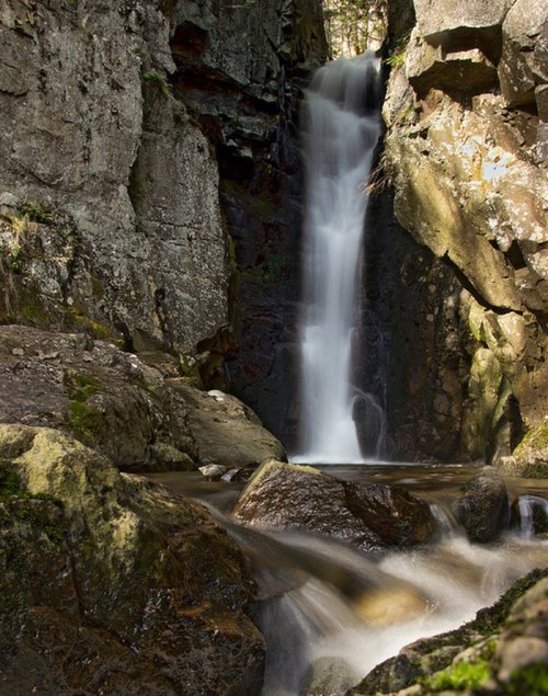 A serene waterfall cascading down rocky cliffs, surrounded by lush greenery and smooth stones in a tranquil setting.
