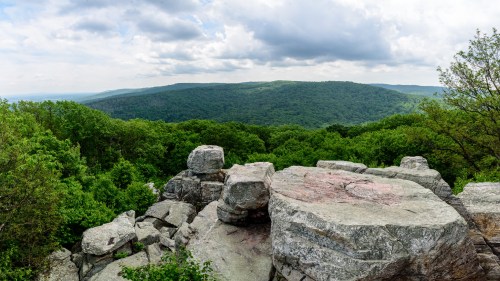 A panoramic view of lush green hills and rocky outcrops under a cloudy sky.