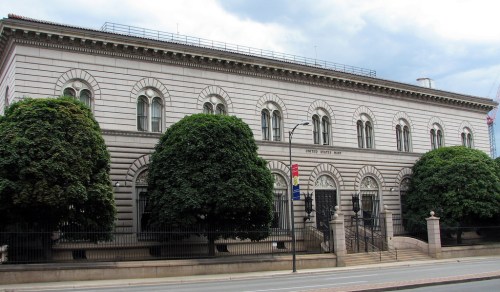 Historic building with ornate architecture, large windows, and lush green trees in front.