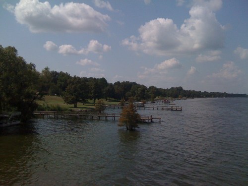 A serene lake view with wooden docks extending into the water, surrounded by trees and fluffy clouds in the sky.