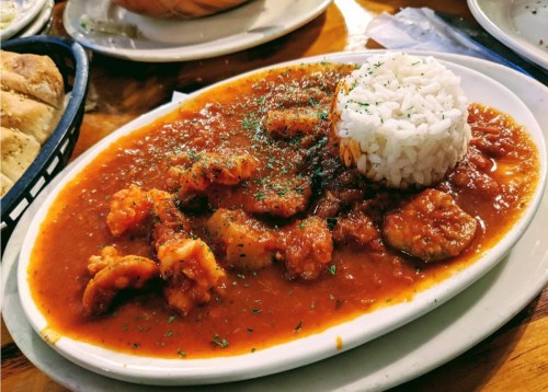 A plate of shrimp in a spicy red sauce, served with a mound of white rice and garnished with herbs.