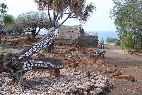 A rocky path leads to a thatched hut by the ocean, with signs warning visitors about the area.