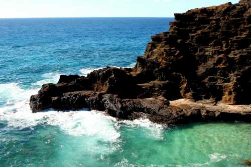 Rocky coastline with turquoise water and waves crashing against the shore under a clear blue sky.