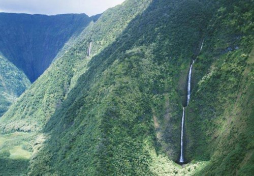 Aerial view of lush green mountains with two cascading waterfalls flowing down steep cliffs.