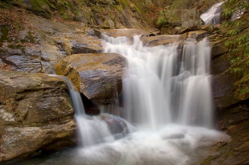 A serene waterfall cascading over smooth rocks, surrounded by lush greenery and natural beauty.