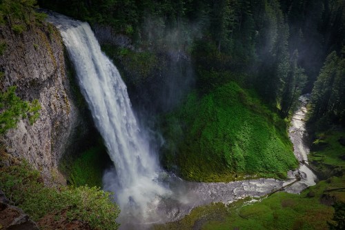 A majestic waterfall cascades down rocky cliffs, surrounded by lush green vegetation and a winding river below.