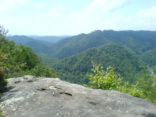 A scenic view of lush green mountains under a bright blue sky, with a rocky foreground.