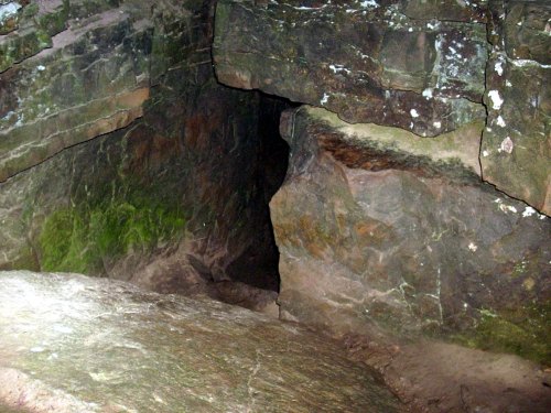 A dark cave entrance surrounded by rugged, moss-covered rock formations.