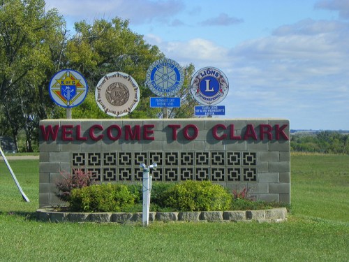 Welcome sign for Clark, featuring various local organization emblems and a green landscape in the background.