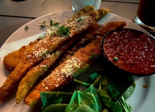 Plate of crispy fried zucchini sticks topped with cheese, served with marinara sauce and fresh spinach on the side.