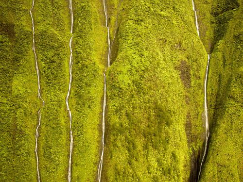 Lush green mountains with cascading waterfalls flowing down their steep, textured surfaces.