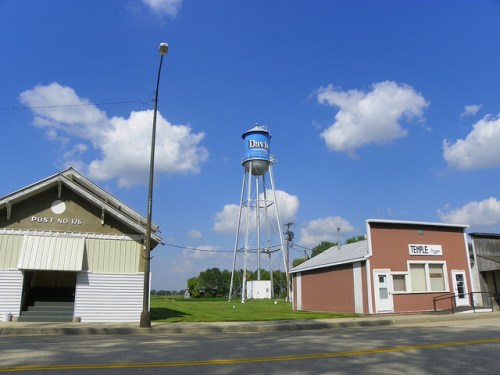 A blue water tower labeled "Davis" stands beside two buildings under a bright blue sky with fluffy clouds.