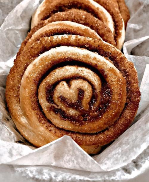 Close-up of freshly baked cinnamon rolls with a golden-brown swirl, resting in parchment paper.