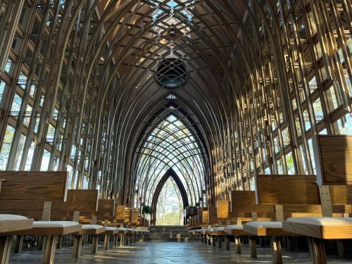 Interior of a modern glass and wood chapel, featuring arched ceilings and rows of wooden benches.