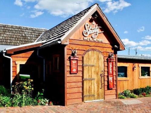 A charming wooden building with a sloped roof, featuring a sign that reads "Shanty" and colorful flowers in front.