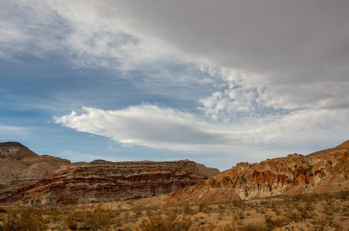 A desert landscape featuring layered rock formations under a cloudy sky.