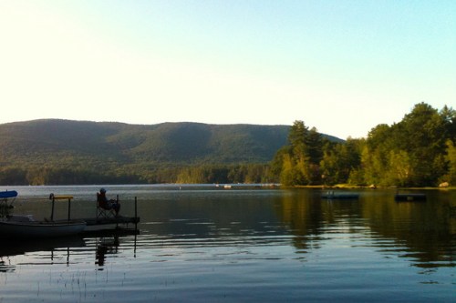 A serene lake surrounded by mountains and trees, reflecting the calm water under a clear sky.
