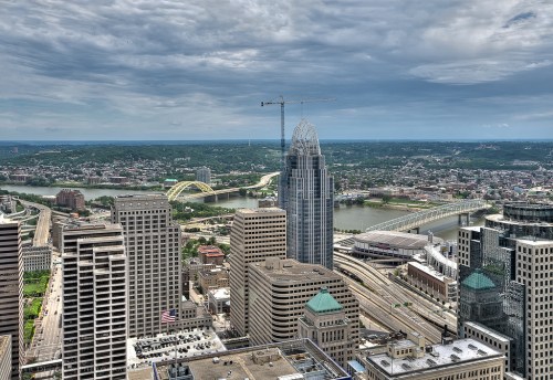 Aerial view of a city skyline with tall buildings, a river, and a bridge under a cloudy sky.