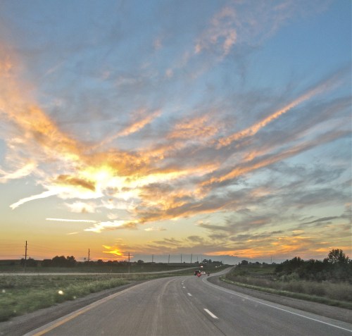 A winding road under a colorful sunset with clouds and a clear sky in the background.