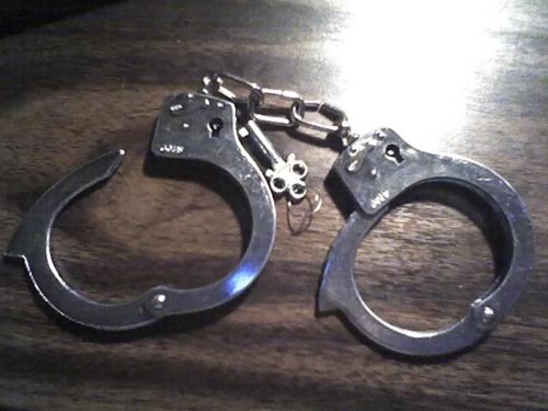 A pair of silver handcuffs resting on a wooden surface.