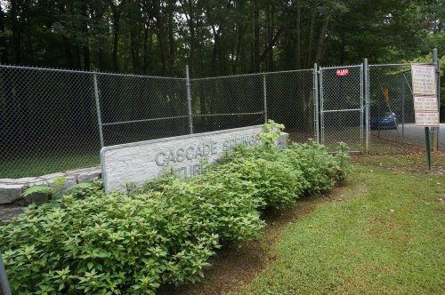 A stone sign reading "Cascade Springs" near a fenced area with greenery and trees in the background.