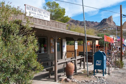 A rustic post office in Oatman, Arizona, with mountains in the background and colorful flags nearby.