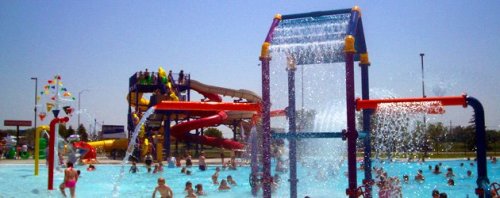 A vibrant water park scene with children playing in a pool, water slides in the background, and colorful water features.