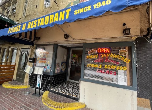 Exterior of Please U Restaurant, featuring a blue awning and a sign advertising sandwiches, seafood, and salads.