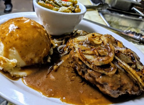 A plate featuring meatloaf with gravy, sautéed onions, mashed potatoes, and a side of green beans.