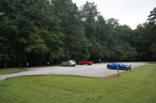 A nearly empty parking lot surrounded by trees, featuring a red truck and a blue car.