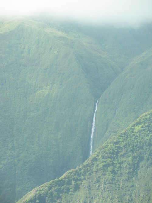 A distant waterfall cascading down lush green mountains, shrouded in mist.