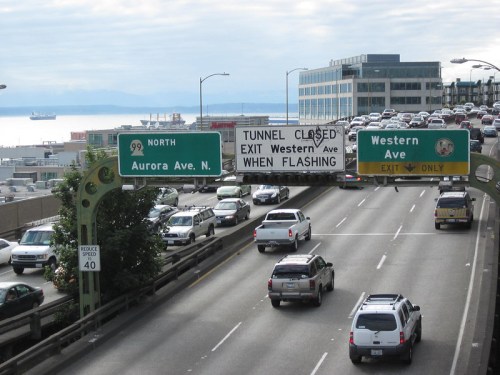 Traffic signs on a highway indicate "Tunnel Closed" and direct drivers to exit at Western Ave, with vehicles on the road.