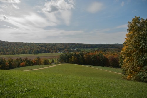 A scenic view of rolling hills and colorful autumn trees under a partly cloudy sky.