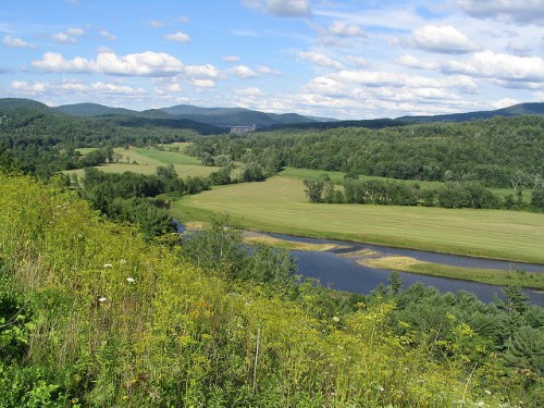 A scenic view of rolling green hills, a winding river, and a blue sky with fluffy clouds.