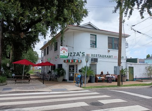 A white restaurant building with red umbrellas outside, featuring a sign that reads "Luzza's Restaurant."