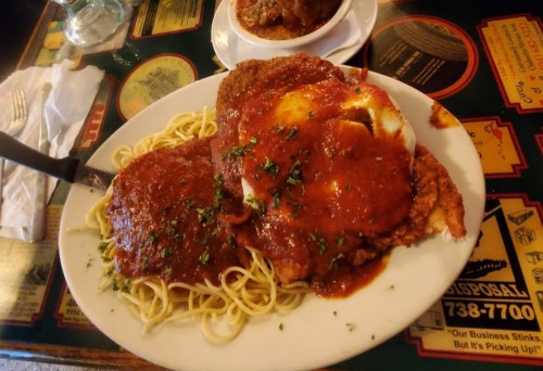 A plate of spaghetti topped with two breaded chicken cutlets and marinara sauce, garnished with parsley.