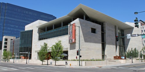 Modern architectural building with large windows and a distinctive roof, surrounded by trees and city streets.