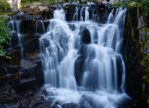 A serene waterfall cascading over rocks, surrounded by lush greenery and natural beauty.
