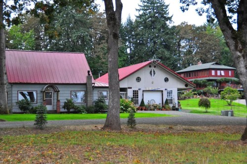 Two distinct houses with red roofs surrounded by trees and greenery, set in a peaceful rural landscape.