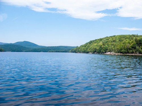 A serene lake surrounded by green hills under a clear blue sky, with gentle ripples on the water's surface.